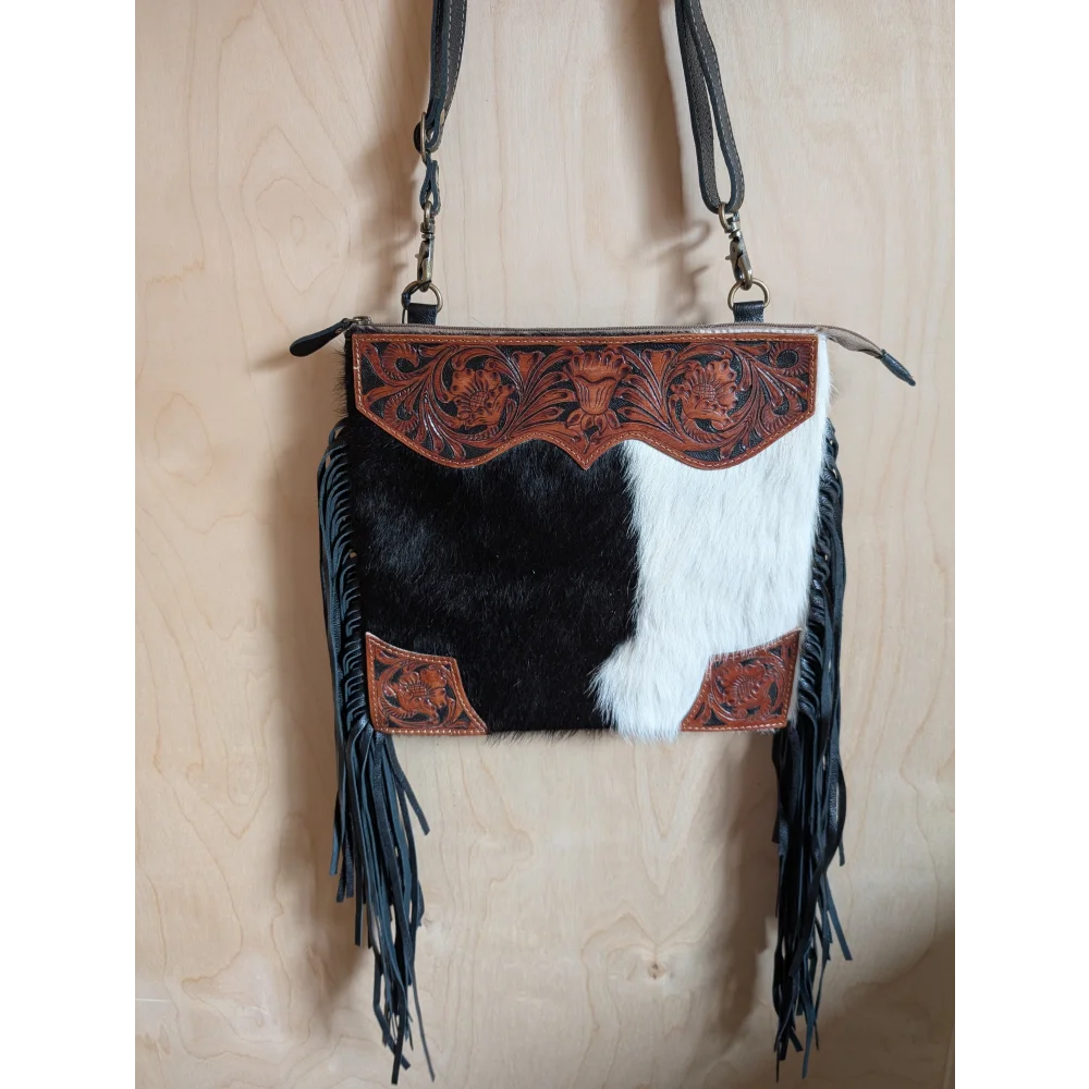 Tumbleweed 5 black and white cowhide crossbody bag with hand tooled brown floral embroidery and smoky charcoal fringes with zippered pocket