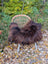 A massive natural dark rusty icelandic sheepskin wool throw draped over a woven wicker chair with white metal legs