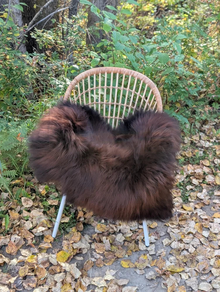 A plush dark rusty icelandic sheepskin throw draped over a woven rattan chair with white metal legs