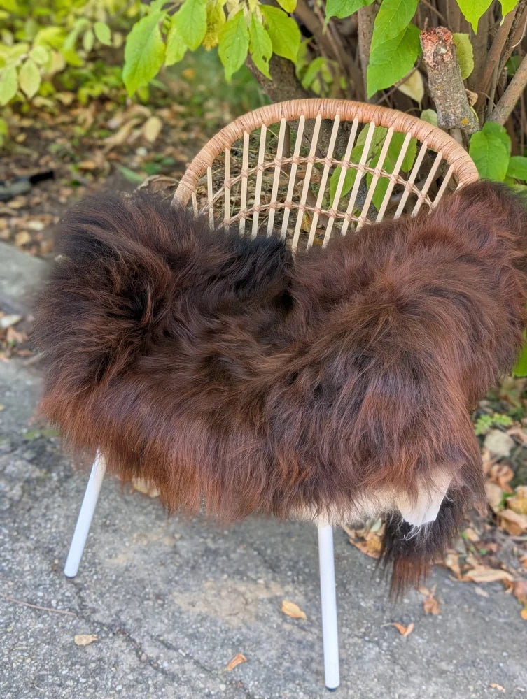 A cozy thick brown wool icelandic sheepskin throw draped over a woven rattan chair with white metal legs