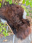 A plush large 49 x 31 natural dark rusty icelandic sheepskin rug with tri-color wool draped over a wicker chair