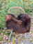 A cozy large natural dark rusty icelandic sheepskin throw draped over a rattan chair with white metal legs