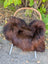 A plush dark rusty icelandic sheepskin rug with soft wool texture on a wicker chair seat for cozy comfort