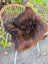 A plush deep brown natural dark rusty icelandic sheepskin with thick wool texture on a woven wicker chair
