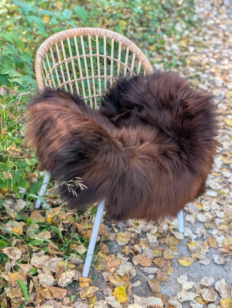 A plush dark rusty icelandic sheepskin throw draped over a wicker chair with white metal legs