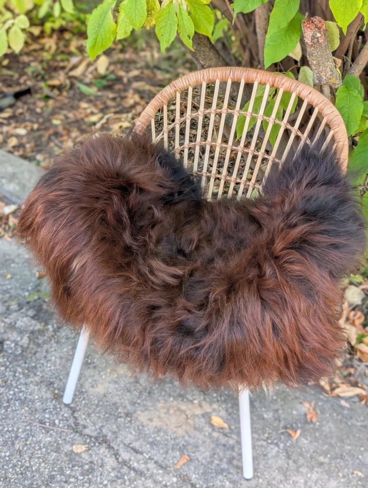 Thick fluffy natural dark rusty icelandic sheepskin draped over wicker chair with white metal legs for cozy seating