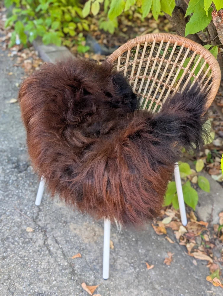 A plush dark brown wool icelandic sheepskin throw draped over a wicker chair with white metal legs