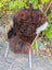 A large 49 x 31 inch natural dark rusty curly wool icelandic sheepskin draped over a wicker chair with metal legs