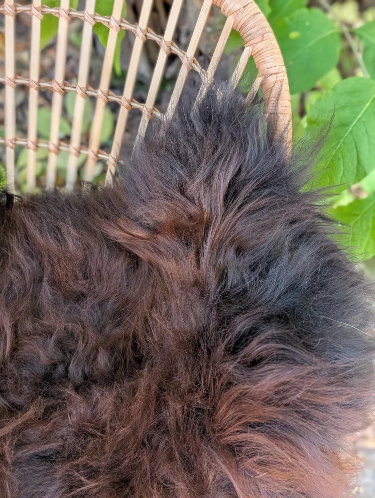A large fluffy dark rusty icelandic sheepskin wool throw draped on a woven wicker chair perfect cozy blanket