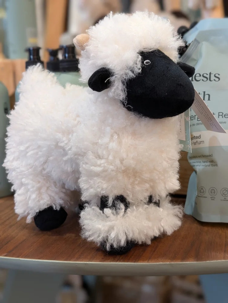 A plush valais sheep by nana huchy in white with black face and feet made from soft fluffy material