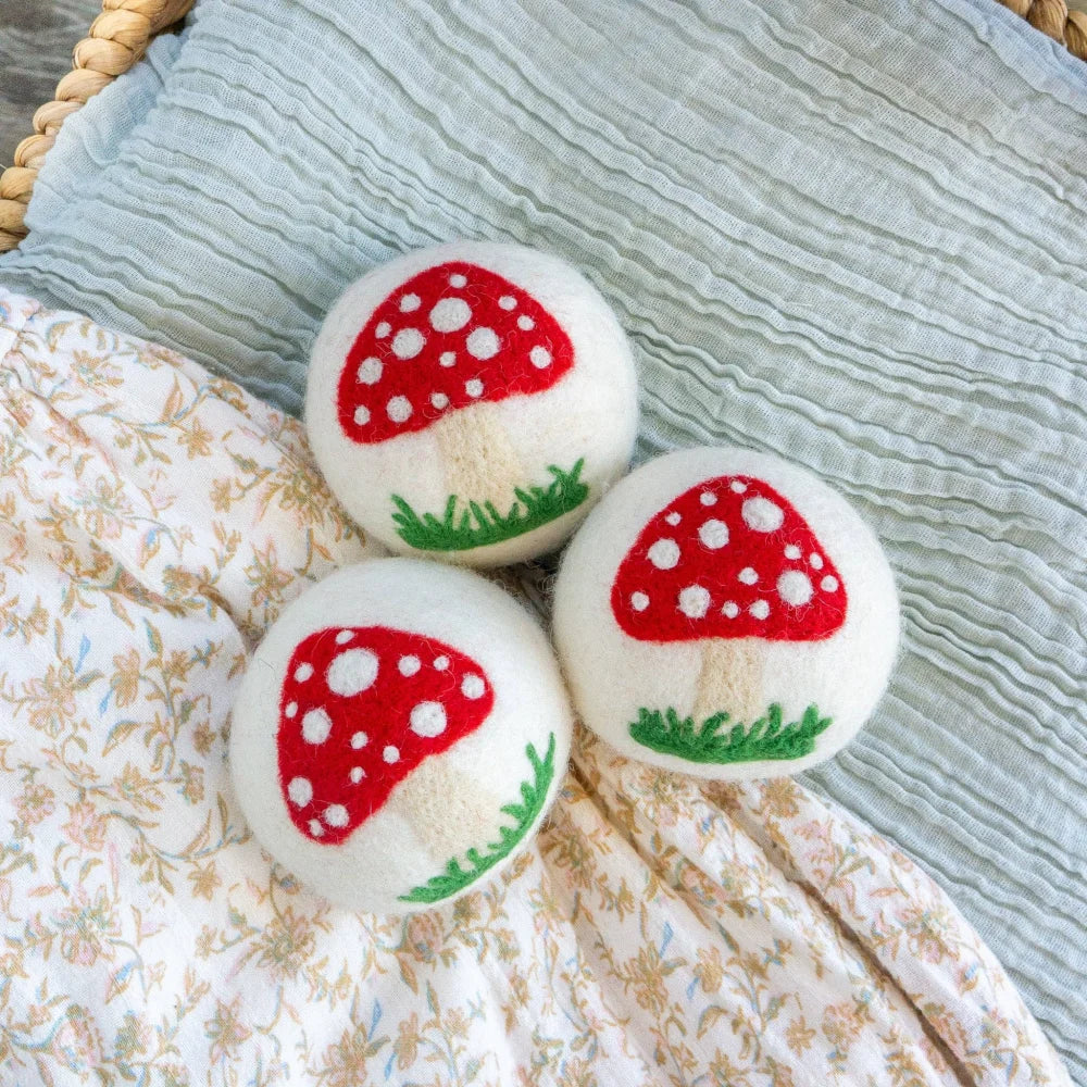 Three fluffy white wool dryer balls embroidered with red mushroom caps and green grass by angus oliver