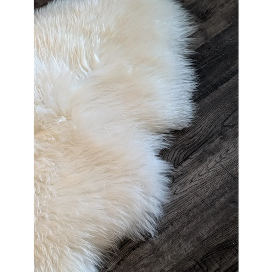A soft white icelandic sheepskin rug 48 x 31 inches with a fluffy texture on a dark wooden floor