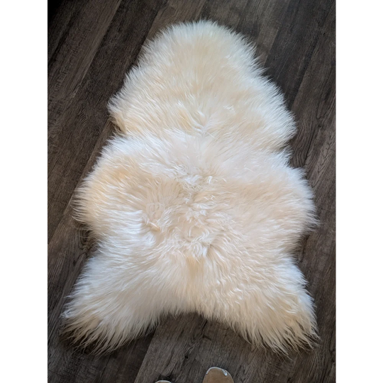 Cream-colored soft icelandic sheepskin rug with dense fur and natural shape, perfect for cozy home decor 48 x 31 inches
