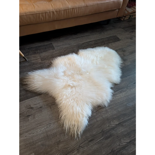 A soft icelandic sheepskin rug in off-white with long fur on a dark wood floor perfect for cozy home decor