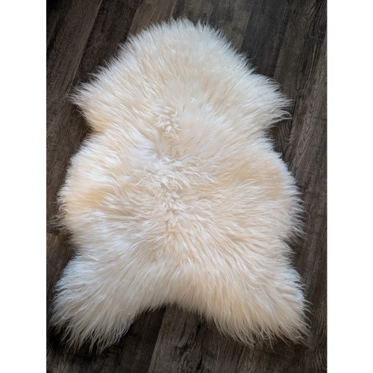 A plush off-white soft icelandic sheepskin rug 48 x 32 inches on a dark wooden floor for cozy decor