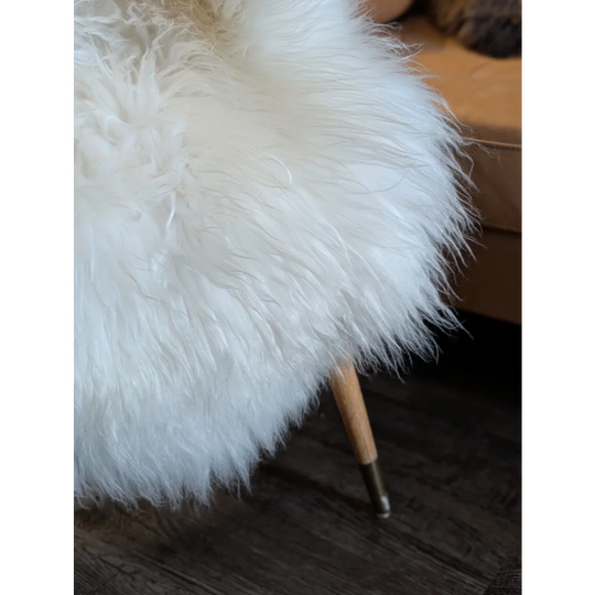 White fluffy stool covered in soft icelandic sheepskin with slender wooden legs and brass tips perfect for cozy spaces