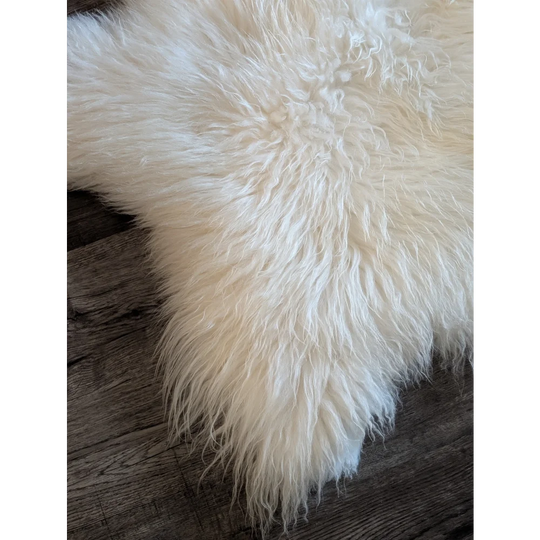 A soft off-white icelandic sheepskin rug with long curly fibers resting on a dark wooden surface 53x34 inches