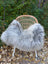 A plush long wool icelandic sheepskin throw in natural grey draped over a woven rattan chair with white metal legs