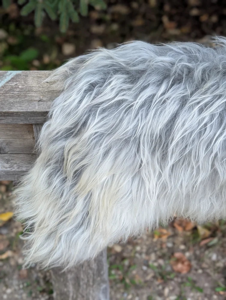 A fluffy long wool icelandic sheepskin throw in natural grey draped over a wooden surface