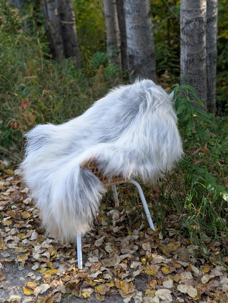 A fluffy white faux fur chair with woven wicker seat and metal legs outdoors featuring a massive icelandic sheepskin
