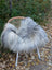 A plush long wool icelandic sheepskin throw in natural grey draped over a woven rattan chair with white legs