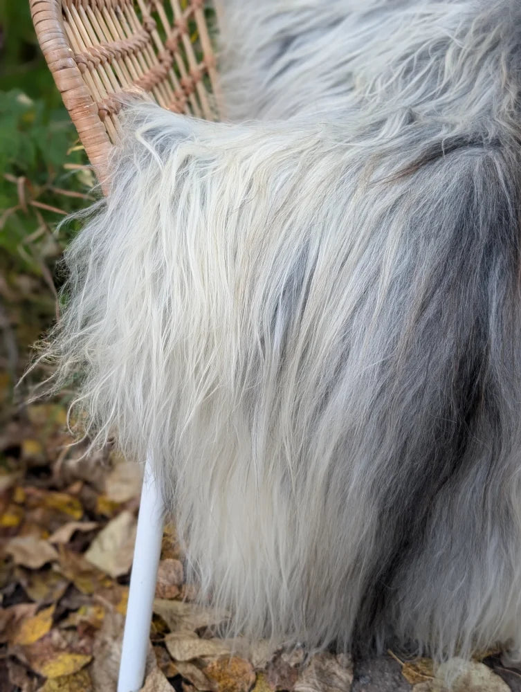 A plush long wool icelandic sheepskin throw in natural grey draped over a wicker chair backrest