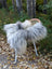 A plush long wool icelandic sheepskin throw in natural grey draped over a woven chair with light legs
