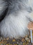 A fluffy gray and white long wool dog sitting on a woven chair with a massive natural grey icelandic sheepskin