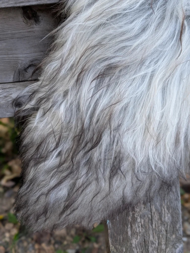 A thick shaggy gray and white massive icelandic sheepskin draped over a wooden post showcasing natural wool icelandic sheepskins