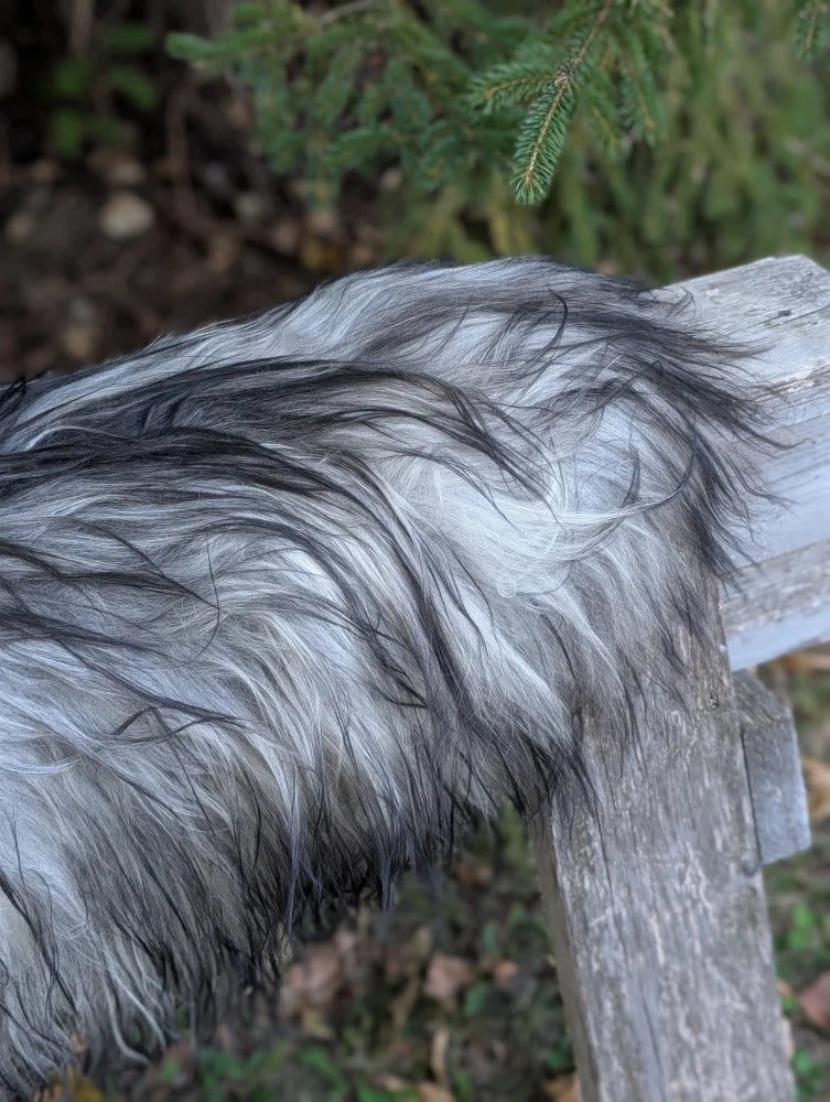 A fluffy dog rests on a weathered fence beside a massive icelandic sheepskin natural grey rug