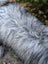 A fluffy silver and black long-haired dog resting on a massive icelandic sheepskin natural grey rug