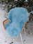 A soft light blue faux fur throw draped over a wicker chair featuring winter blue green merino sheepskin style