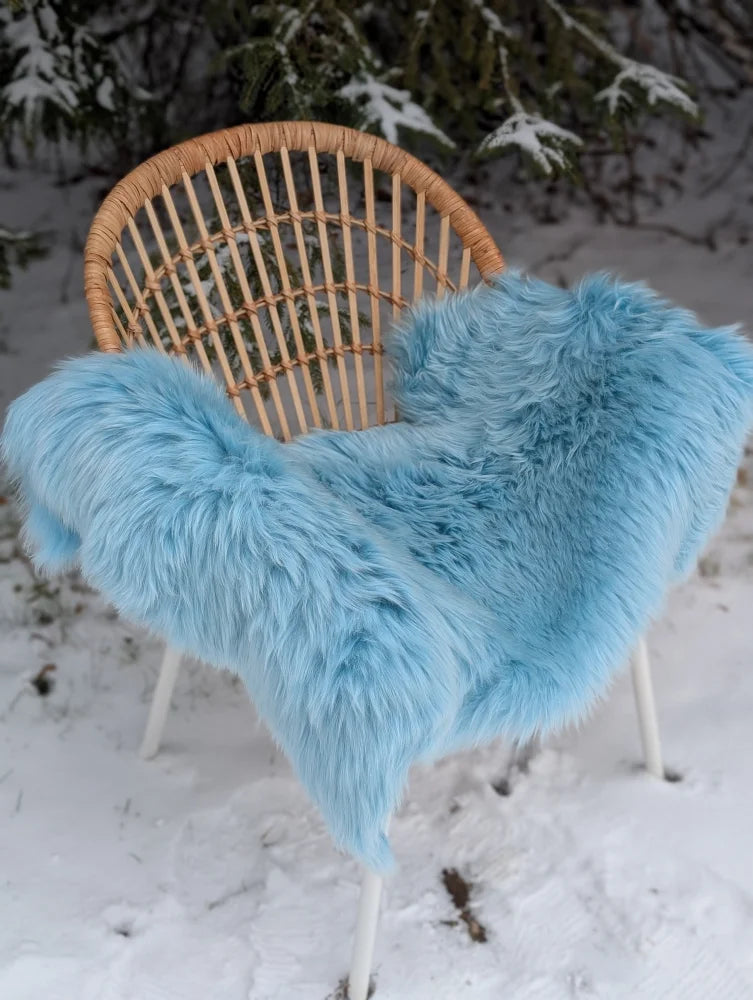 A soft light blue faux fur throw draped over wicker chair featured with green merino sheepskin accents