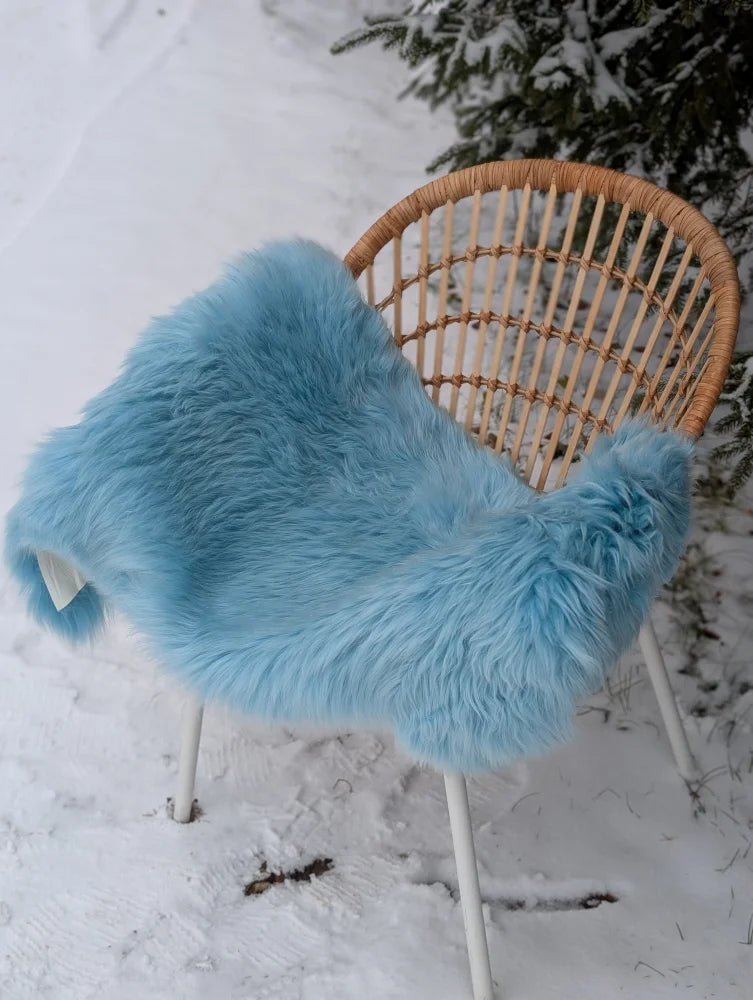 A soft light blue faux fur throw draped over a wicker chair featuring cozy minty green merino sheepskin accents