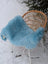 A soft light blue faux fur throw draped over a wicker chair featuring cozy minty green merino sheepskin accents