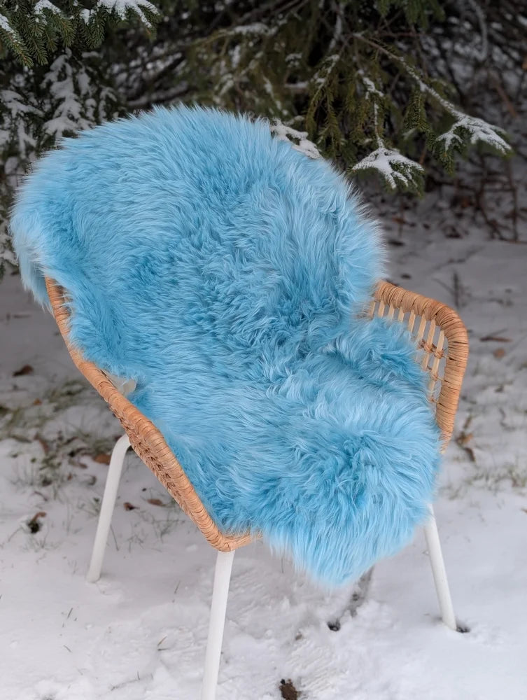 A plush minty green merino sheepskin throw draped over a wicker chair with white legs perfect for winter cozy vibes