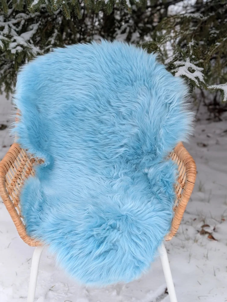 A plush light blue sheepskin rug draped over a wicker chair perfect as a green merino sheepskin accent piece