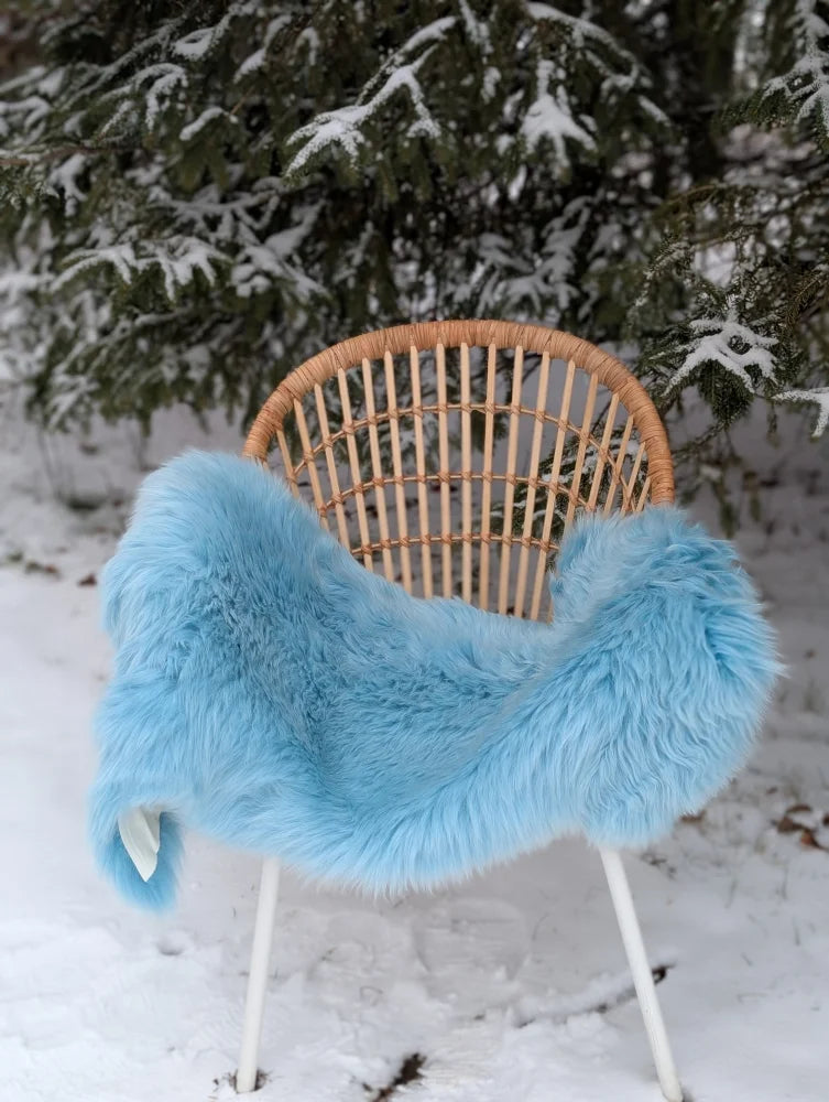 Light blue faux fur throw draped over wicker chair showing soft minty green merino sheepskin texture