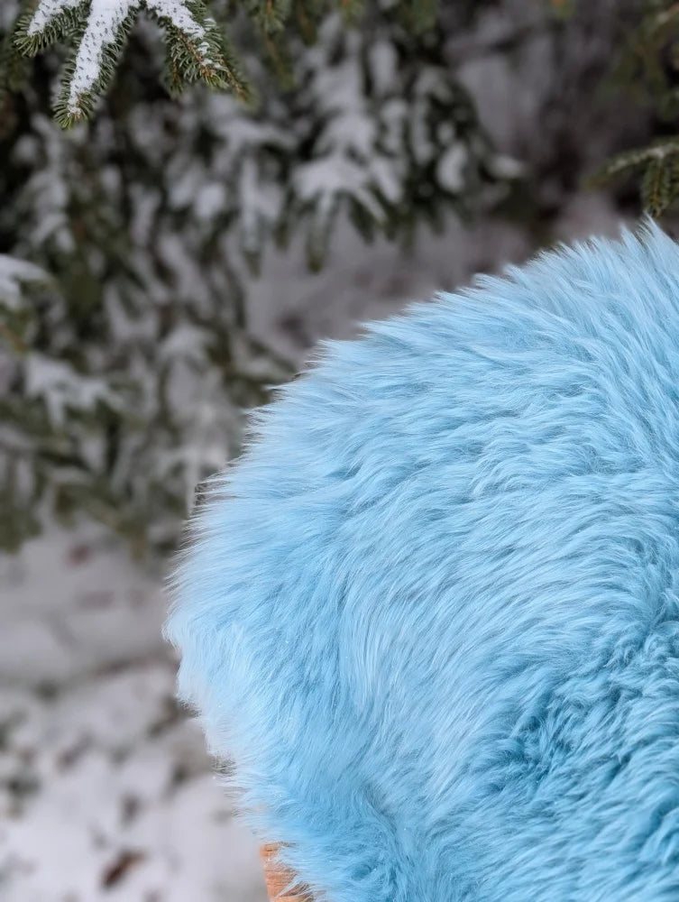 A soft light blue circular cushion with fluffy texture made from green merino sheepskin perfect for winter decor