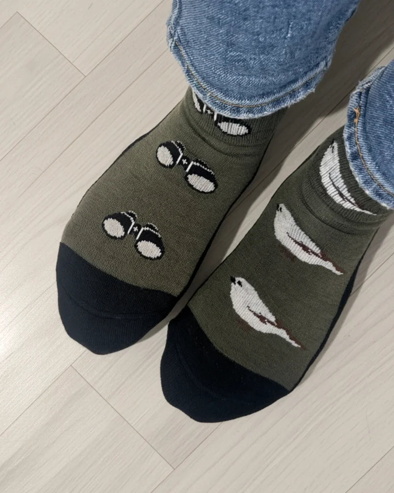 Olive green merino wool crew socks with black toe caps and white bird and glasses designs for all-season wear
