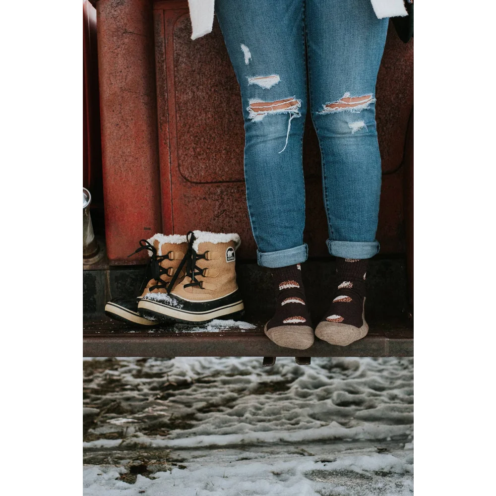 Tan sorel snow boots with black laces and white sole next to ripped jeans paired with breathable merino wool socks