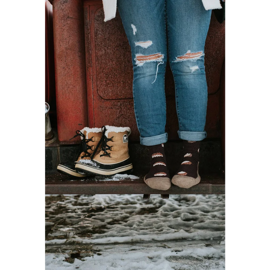Tan sorel snow boots with black laces and white sole next to ripped jeans paired with breathable merino wool socks
