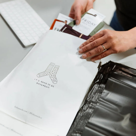 White paper shopping bag with black line drawing of striped and polka-dotted ladybug merino wool socks and text its good to be different