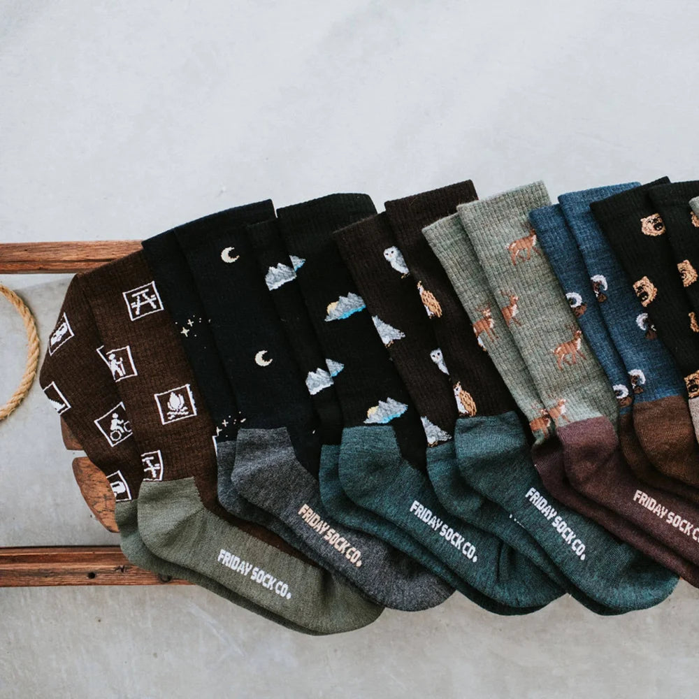 A collection of cozy earthy toned womens skunk merino wool socks from friday sock co with whimsical designs like owls bears and campfires