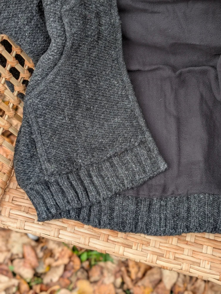 A cozy dark gray calgary cardigan made from zealand wool with a ribbed hem and textured weave on a basket