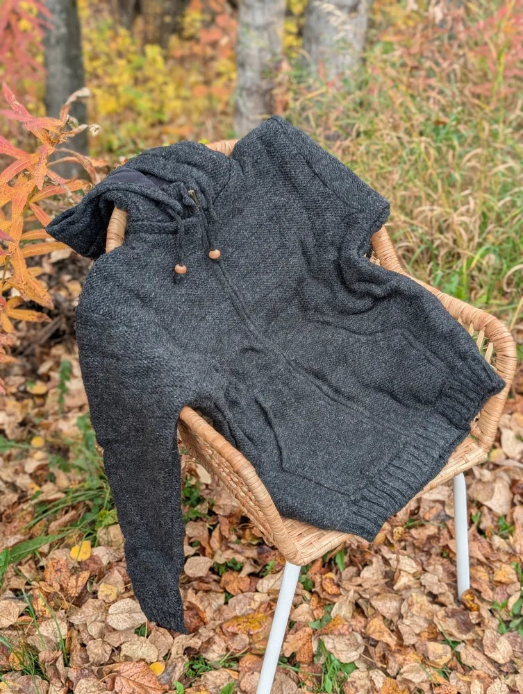 Dark gray calgary cardigan woolen hoodie with zealand wool and attached hood resting on a wicker chair