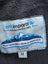 A light gray woven label with blue text and mountain design on the woolen calgary cardigan made with 100% new zealand wool and attached hood