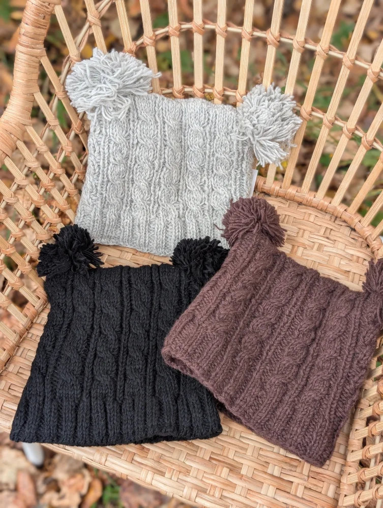 Three woolen heelah double pompom hats in gray black and brown with cable knit patterns and fluffy pom poms