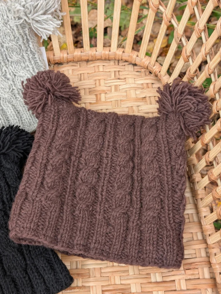 A cozy brown woolen heelah double pompom hat with cable knit texture and fluffy double pompoms on top