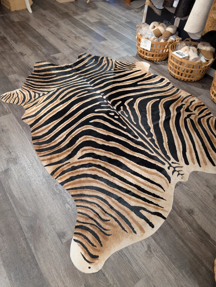 A gorgeous zebra printed large cowhide rug by angus oliver with bold black and tan stripes and unique characteristics on gray wood floor